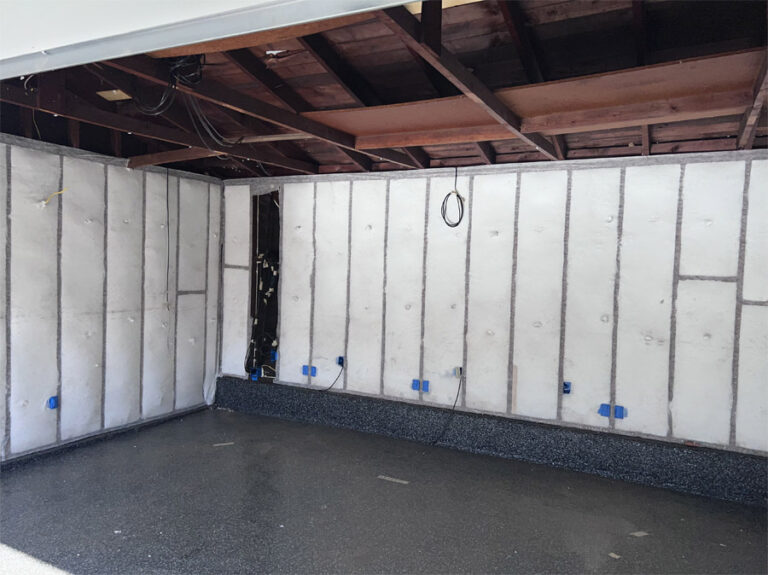 Interior view of a garage with walls covered in white insulation panels and visible rafters, highlighting the steps taken to improve thermal efficiency.