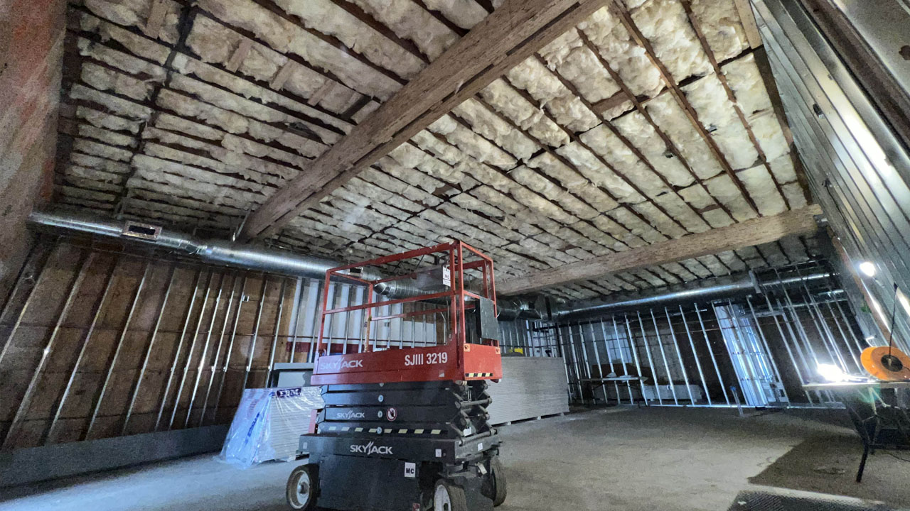 A wide view of a building under renovation with extensive insulation work, highlighting the open rafters and installed fiberglass on the ceiling and walls.