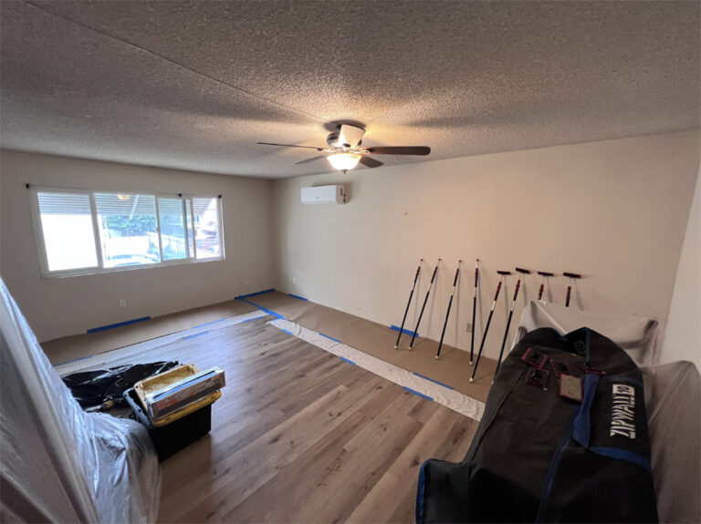 A room nearing completion with walls and ceilings insulated, floors laid with light wood, and protective sheeting on the walls indicating final stages of construction.
